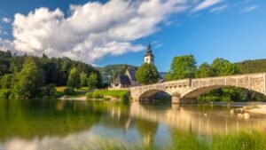 Long exposure sunny nature landscape with mountain lake in Slovenia. beautiful lake Bohinj with perfect sky at summer. view on calm lake with azure water, church and stone bridge on backgr...