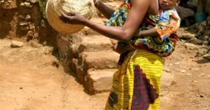 Woman in Yellow Dress Carrying Child and Working in Village