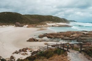 Amazing scenery on wide sandy Lights Beach with rocky formations and grassy hill washing by foamy ocean against cloudy sky in Albany