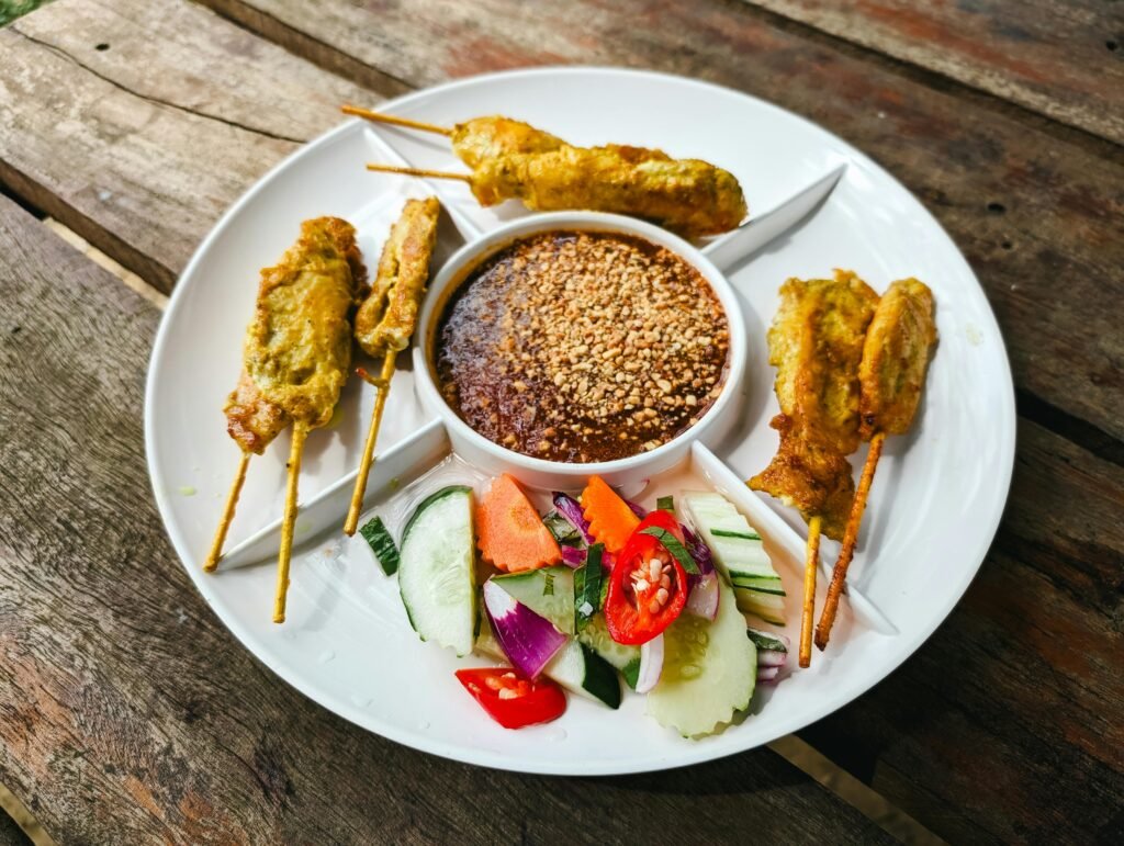 Close-up of chicken satay skewers served with peanut sauce and fresh vegetables.