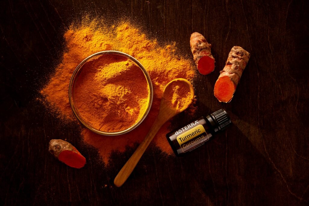 Top view of turmeric powder, turmeric roots, and essential oil on wooden surface.