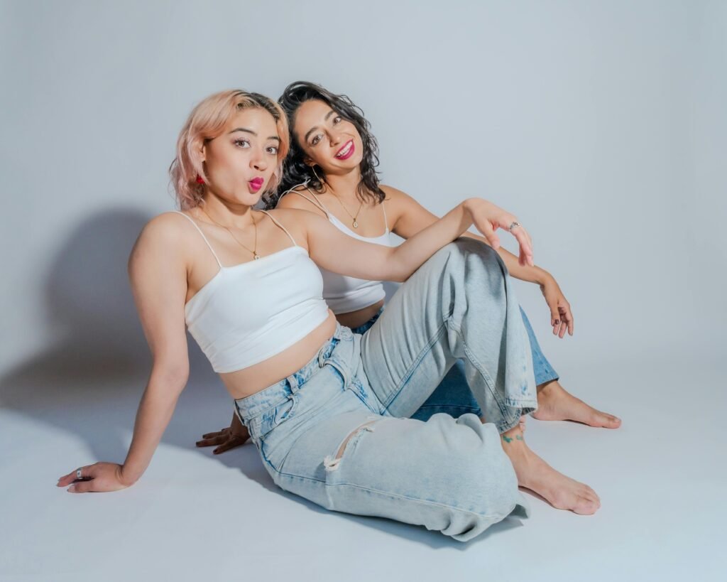 Two young women in casual attire sit together, showcasing friendship and style.