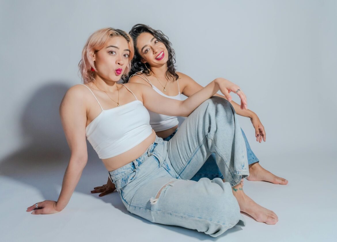 Dos mujeres jóvenes vestidas de manera informal se sientan juntas, mostrando amistad y estilo.