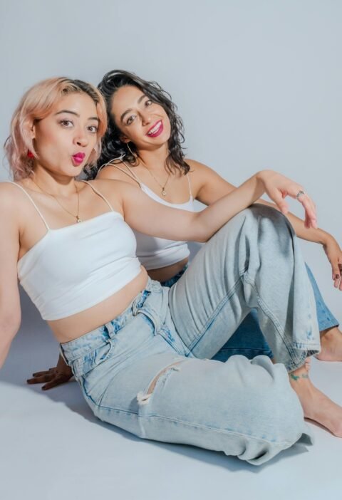 Two young women in casual attire sit together, showcasing friendship and style.