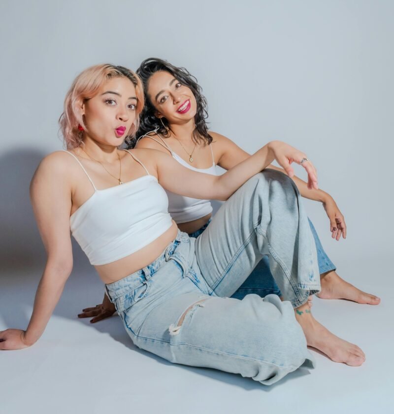 Two young women in casual attire sit together, showcasing friendship and style.