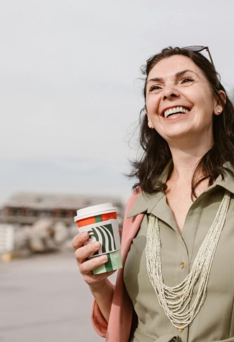 Smiling women enjoying conversation and coffee outdoors on a sunny day, promoting connection and lifestyle.