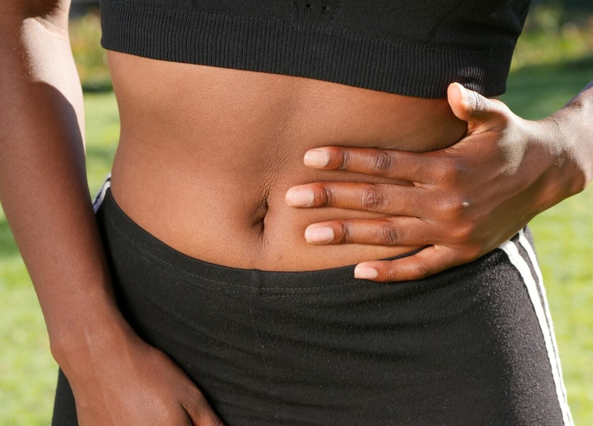 Close-up of a person holding their abdomen, indicating stomach discomfort, outdoors.